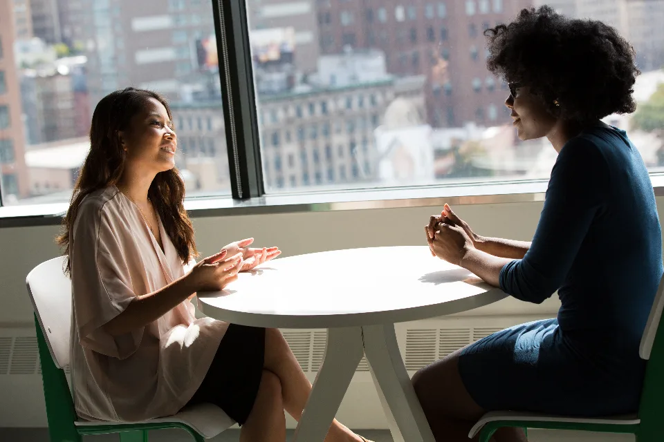 Two colleagues talking across a table by a window